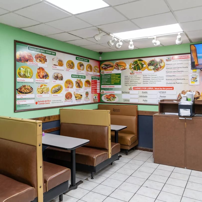 Interior of a Mexican restaurant with brown booths, tables, and a large menu board on a green wall.