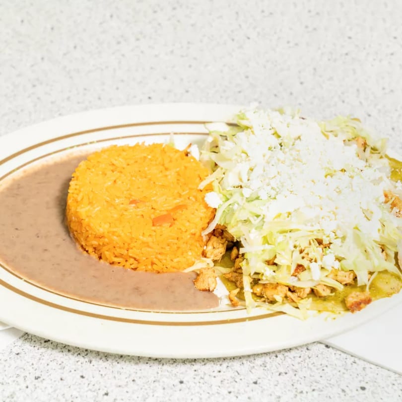A plate of Mexican food with orange rice, refried beans, and chicken enchiladas topped with lettuce and cheese.