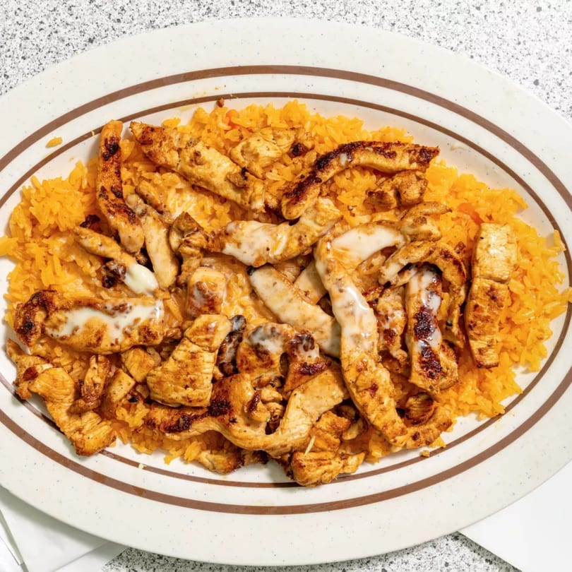 Grilled chicken strips with white sauce and orange rice on an oval plate.