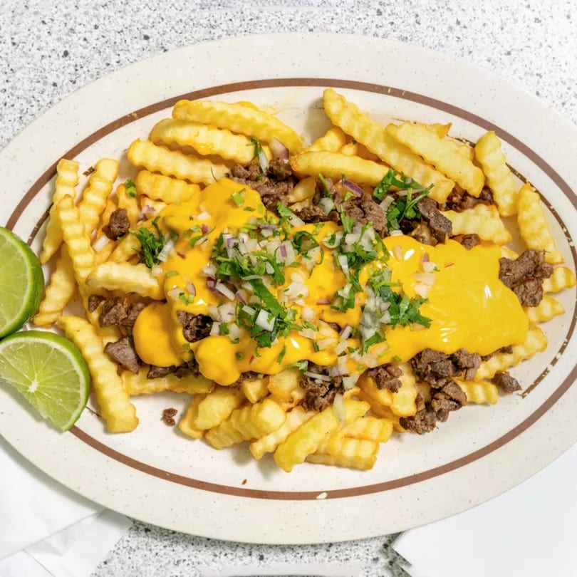 Mexican-style loaded fries with melted cheese, ground beef, diced onions, cilantro, and lime wedges.